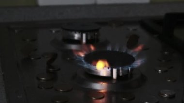 Bozuk paralar, mutfaktaki mavi alevle parlayan gaz yakıcının üzerine düşer.