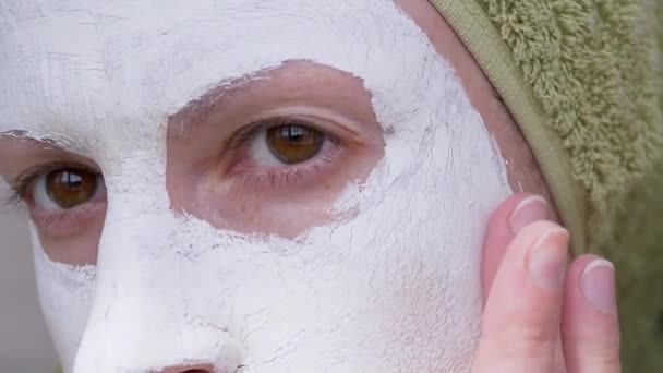 Kvinnan i en vit Clay Mask på ansiktet och en grön handduk på huvudet. Närbild. 4K — Stockvideo