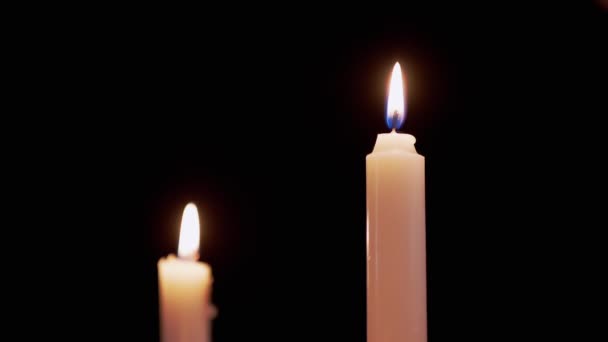 Twee witte Paraffine kaarsen branden met geel vuur, op een zwarte achtergrond. — Stockvideo