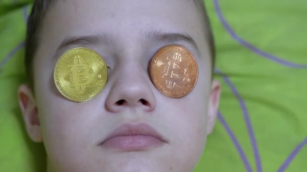 Nastolatek kłamie, na łóżku ze złotymi bitcoinami na oczach. Żarty. Milioner dziecięcy — Wideo stockowe