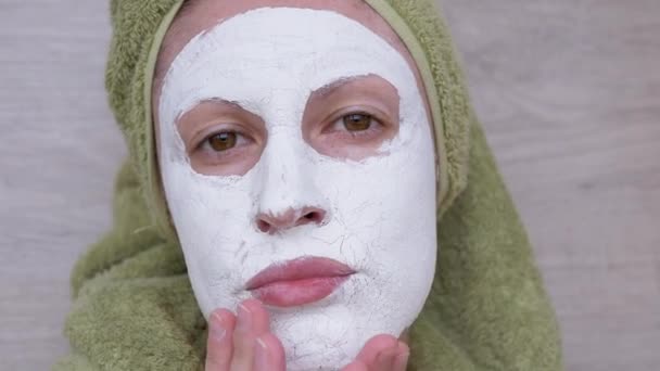 Mujer con una máscara de arcilla blanca en la cara y una toalla verde en la cabeza. Primer plano. 4K — Vídeos de Stock