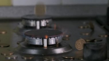 Bozuk paralar, mutfaktaki mavi alevle parlayan gaz yakıcının üzerine düşer.