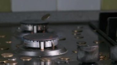 Bozuk paralar, mutfaktaki mavi alevle parlayan gaz yakıcının üzerine düşer.