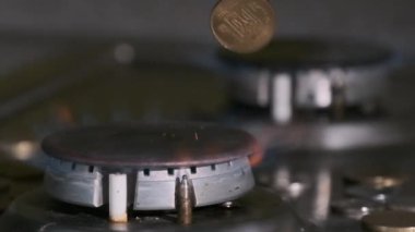 Bozuk paralar, mutfaktaki mavi alevle parlayan gaz yakıcının üzerine düşer.