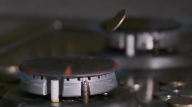 Bozuk paralar, mutfaktaki mavi alevle parlayan gaz yakıcının üzerine düşer.