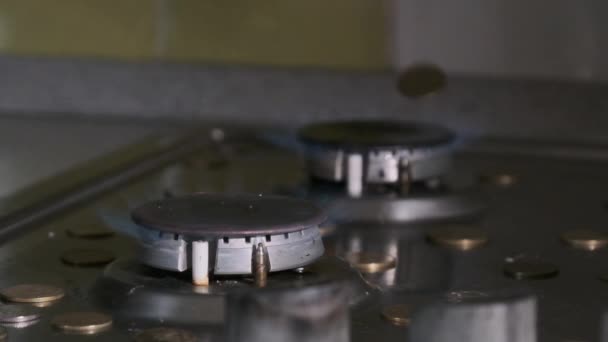 Монеты падают на газовую горелку, которая светится голубым пламенем на кухне — стоковое видео