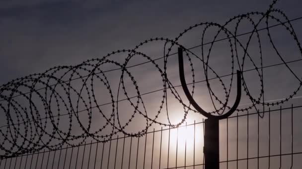 Prikkeldraad hangt aan de grens van een ijzeren hek tegen de achtergrond van zonsondergang. 4K — Stockvideo