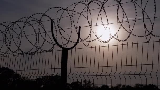 Fil barbelé accroche à la frontière d'une clôture de fer dans le contexte du coucher du soleil. 4K — Video