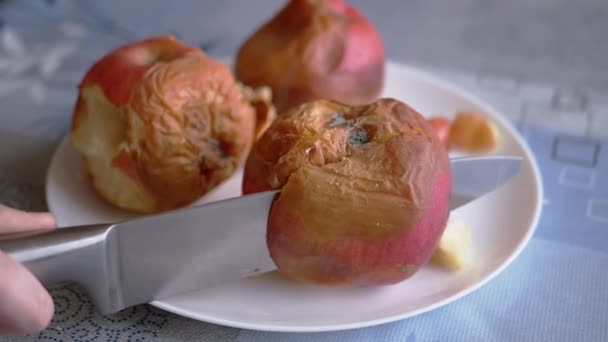 Kvinnlig hand skär ett ruttet äpple på en tallrik med en kniv. Bortskämda, mögliga frukter — Stockvideo