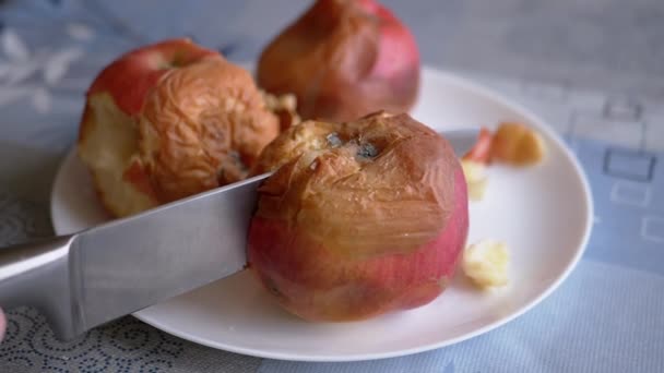 Weibliche Hand schneidet einen faulen Apfel mit einem Messer auf einen Teller. Verdorbene, verschimmelte Früchte — Stockvideo