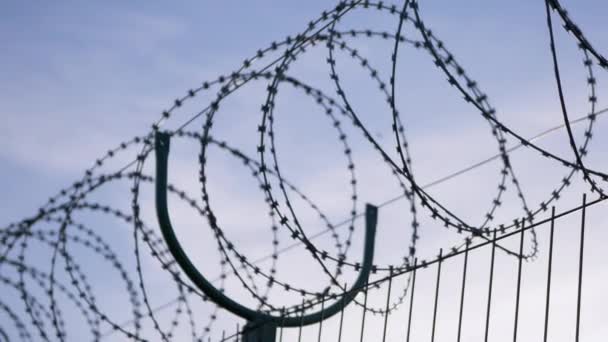 Fil barbelé suspendu à la frontière de la clôture de fer contre le ciel bleu. 4K — Video