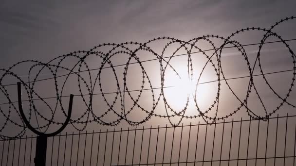Barbed Wire hænger på grænsen af en jernhegn på baggrund af solnedgang. Forstør – Stock-video