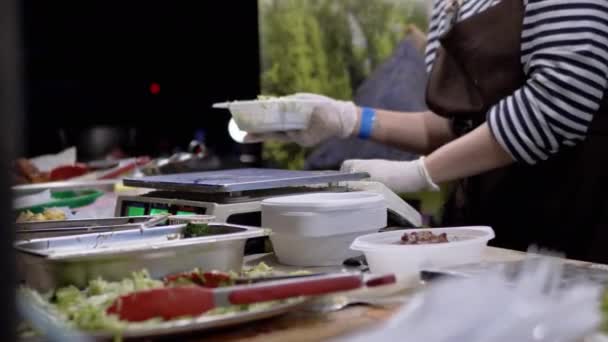 Уличный продавец в резиновых перчатках весит салат в коробке для обедов на электронных весах — стоковое видео