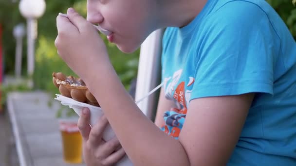 Bambino seduto sulla panchina, mangia gelato cremoso in una tazza di waffle, in un parco in strada — Video Stock