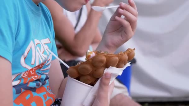 Bambino seduto sulla panchina, mangia gelato cremoso in una tazza di waffle, in un parco in strada — Video Stock