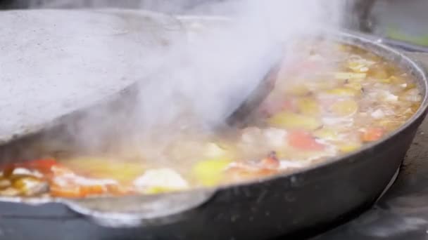 Вуличний шеф-кухар готує овочеве рагу на відкритому повітрі в чавунній сковороді або Wok — стокове відео