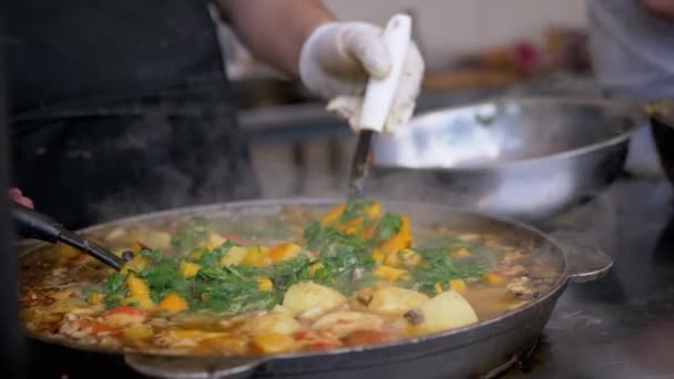 Chef callejero prepara un guiso de verduras al aire libre en una sartén de hierro fundido o Wok — Vídeo de stock