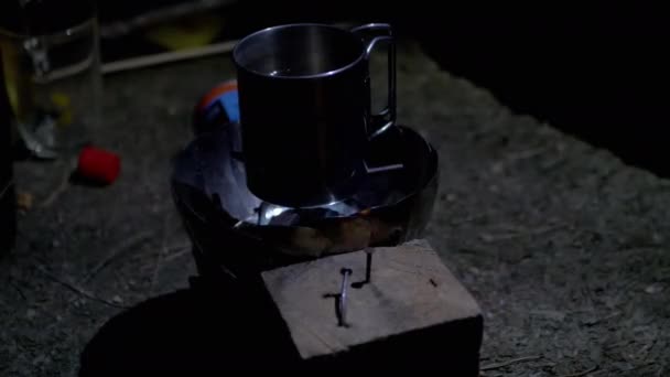 Металлическая кружка с водой нагревается на газовой горелке ночью в лесу. 4K — стоковое видео