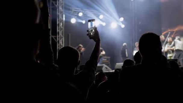 People Record Video on a Smartphone of a Night Rock Concert on Open Stage (en inglés). 4K — Vídeo de stock