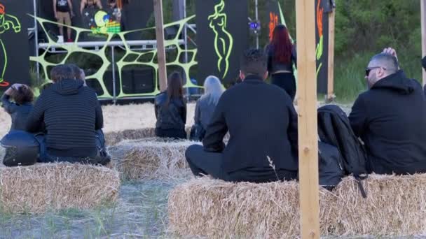 Vista posteriore dei giovani seduti in un fieno e guardando una fase all'aperto. 4K — Video Stock