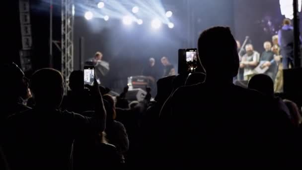 People Record Video on a Smartphone of a Night Rock Concert on Open Stage (en inglés). 4K — Vídeo de stock