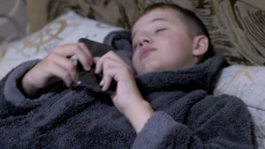 Evde Giyinen Gecelikli Gülümseyen Çocuk elinde Akıllı Telefon ile uykuya dalıyor. 4K