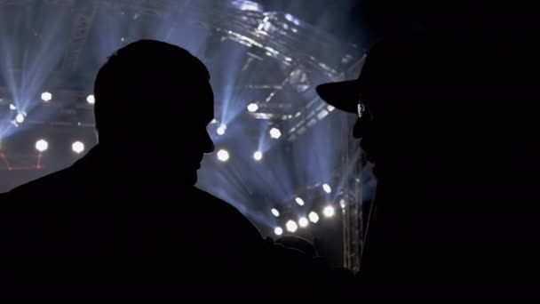 Силуэты двух общительных людей ночью на концерте. 4K — стоковое видео
