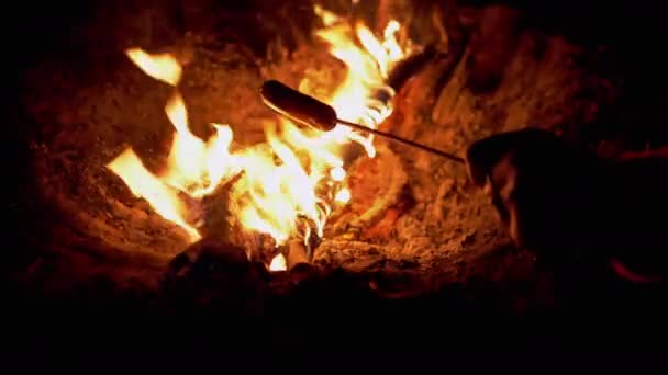 Hungrige Frau grillt Würstchen auf Holzspießen und sitzt am Lagerfeuer. 4K — Stockvideo