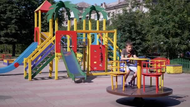 Solitario, Bambino triste rotazione sulla giostra vuota durante la quarantena al parco giochi — Video Stock