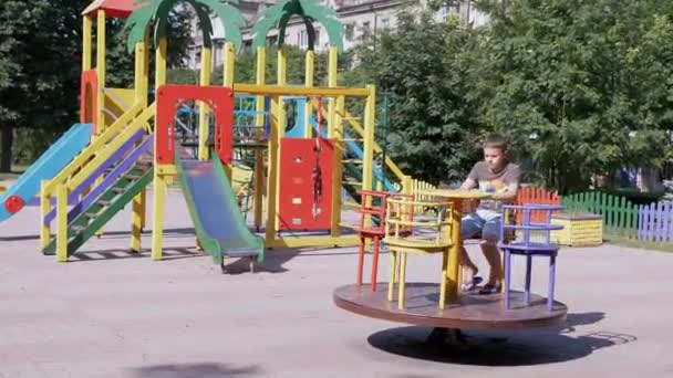 Ensam, Sad Child Rotationing på tom karusell under karantän på lekplatsen — Stockvideo
