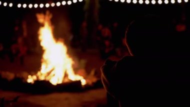 Çocuk, bir grup turistle birlikte ormanda şenlik ateşine bakıyor. 4K