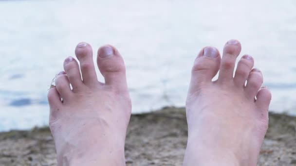 Vrouwen voeten zonnebaden op een zandstrand aan de rivier, in de buurt van het water. 4K — Stockvideo