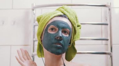 Yüzünde kilden maske olan kız kulaklıkla müzik dinler, tuvalette dans eder.