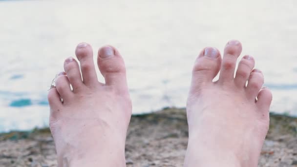 Vrouwen voeten zonnebaden op een zandstrand aan de rivier, in de buurt van het water. 4K — Stockvideo