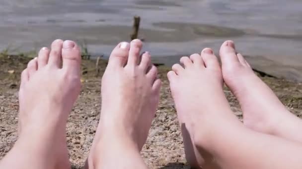 Fötter av kvinnor och barn Sola på en sandstrand vid floden, nära vattnet — Stockvideo