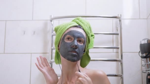 Girl with a Clay Mask on Face Listens to Music on Headphones, Dances in Bathroom — Stock Video