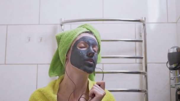 Lány egy Clay Mask on Face zenét hallgat a fejhallgató, Táncok a fürdőszobában — Stock videók