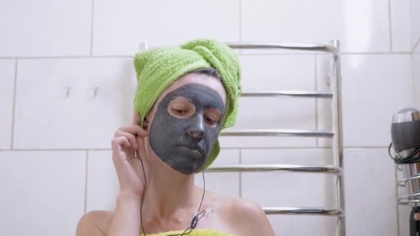 Lány egy Clay Mask on Face zenét hallgat a fejhallgató, Táncok a fürdőszobában — Stock videók