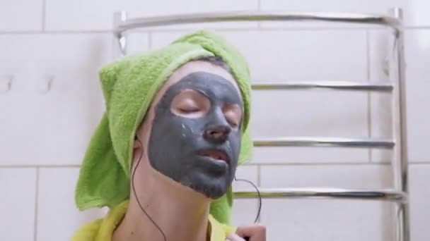 Chica con una máscara de arcilla en la cara Escucha música en los auriculares, Danzas en el baño — Vídeo de stock