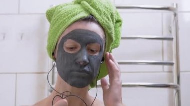 Yüzünde kilden maske olan kız kulaklıkla müzik dinler, tuvalette dans eder.