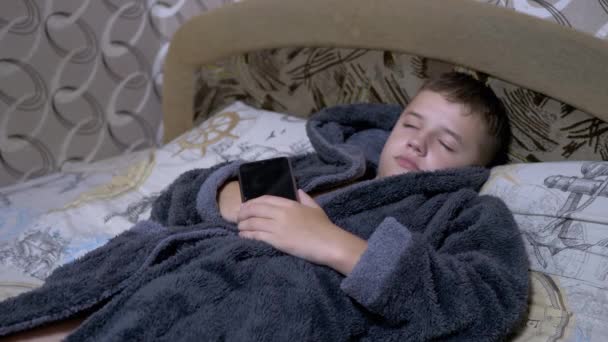 Adorable Child in Home Gray Ddressing Gown Falls Asleep with Smartphone in Hands — стоковое видео