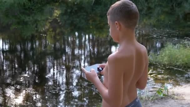 Sad Child站在河岸河边，在森林里玩智能手机。4K — 图库视频影像