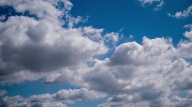 Daylight time-lapse capturing fast-moving white cloud layers drifting across a vibrant, sunny blue sky, showing various soft formations spreading and evolving, creating a serene and airy skyscape background.