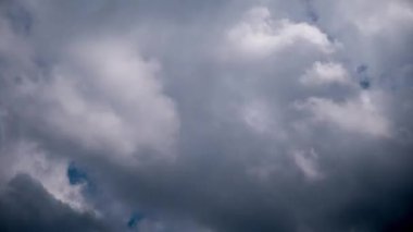 Upward view timelapse of fluffy white cumulus clouds moving quickly across bright blue sky, transforming into dark, heavy storm clouds that completely obscure daylight, signaling approaching bad weather.