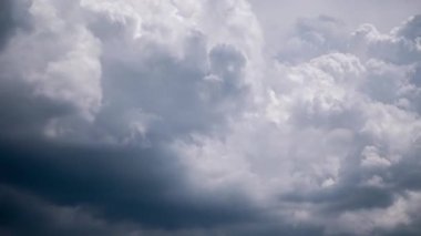 Dramatic timelapse shows bright cumulus clouds rapidly transforming into dark grey storm clouds, revealing turbulent formations and ominous shadows that cover the blue sky, signaling approaching bad weather. 199 chars