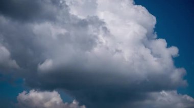 Dramatic timelapse of large grey storm clouds rapidly forming and moving across a deep blue sky, creating a dynamic and foreboding weather pattern with patches of sunlight breaking through.