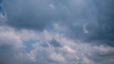 Timelapse shot of dynamic white and grey clouds drifting across a vibrant blue sky, showing shifting light and shadow as birds occasionally fly through the atmospheric daytime scene.