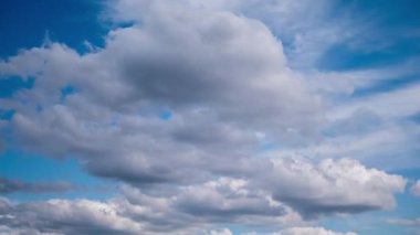 High-speed time-lapse of a layered cloudscape, where wispy high-altitude clouds sweep over lower puffy formations against a clear blue sky, illustrating complex weather patterns and atmospheric change.