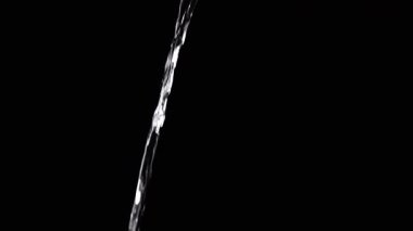 Thin Stream Of Water Pouring On Black Background. Close-up, slow motion. A clear stream of water flows down into empty space. Splashes. Abstract, texture, lighting. Clean water.