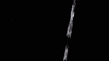 Titreşen bir su akıntısı, sıçramalarla, siyah bir zemin üzerine dökülüyor. Yakın çekim, yavaş çekim. İçinde su damlaları olan şeffaf bir dere boşluğa akar. Damlalar, damlalar. Soyutlama, doku.